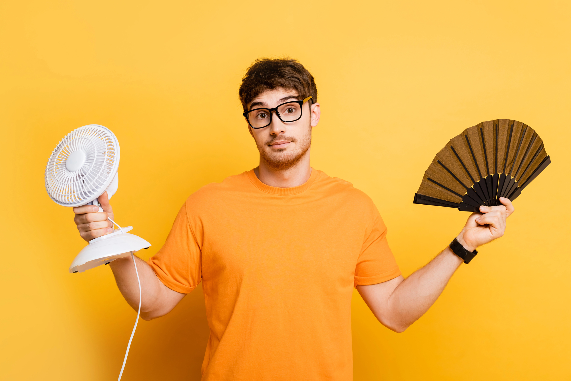 Homme hésitant entre un ventilateur électrique et un éventail pour mieux vivre avec la chaleur